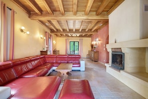 A living room with a wooden ceiling, a fireplace, a red leather sofa, and a dining area.