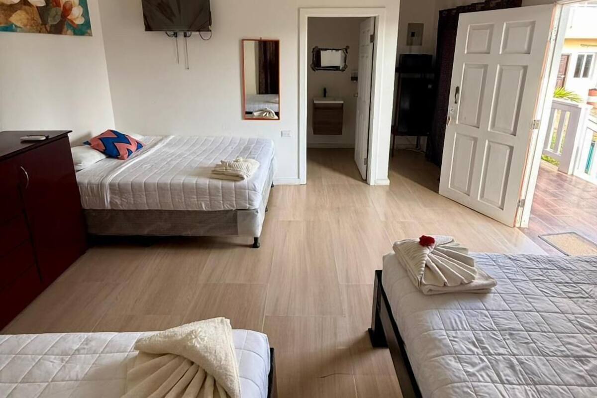 Habitación de hotel con dos camas, un televisor, un cuadro y un baño visible a través de una puerta abierta.