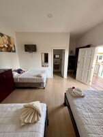 Habitación de hotel con dos camas, un televisor, un cuadro y un baño visible a través de una puerta abierta.