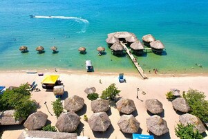 Vista aérea de una playa con cabañas de techo de paja, agua turquesa cristalina y una orilla arenosa.