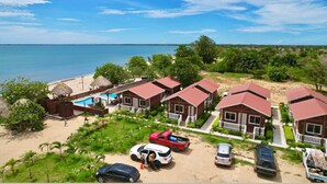 Un complexe hôtelier en bord de mer comprenant plusieurs chalets en bois, une piscine et un espace de plage.