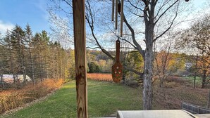 Une terrasse en bois avec une rambarde en métal, une mangeoire à oiseaux suspendue et une vue sur une cour verdoyante avec des arbres.