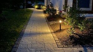 A pathway leading to a house with a lit entrance and a small garden area.