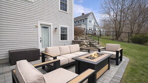 A patio with a sofa set, a fire pit, and a stone wall.