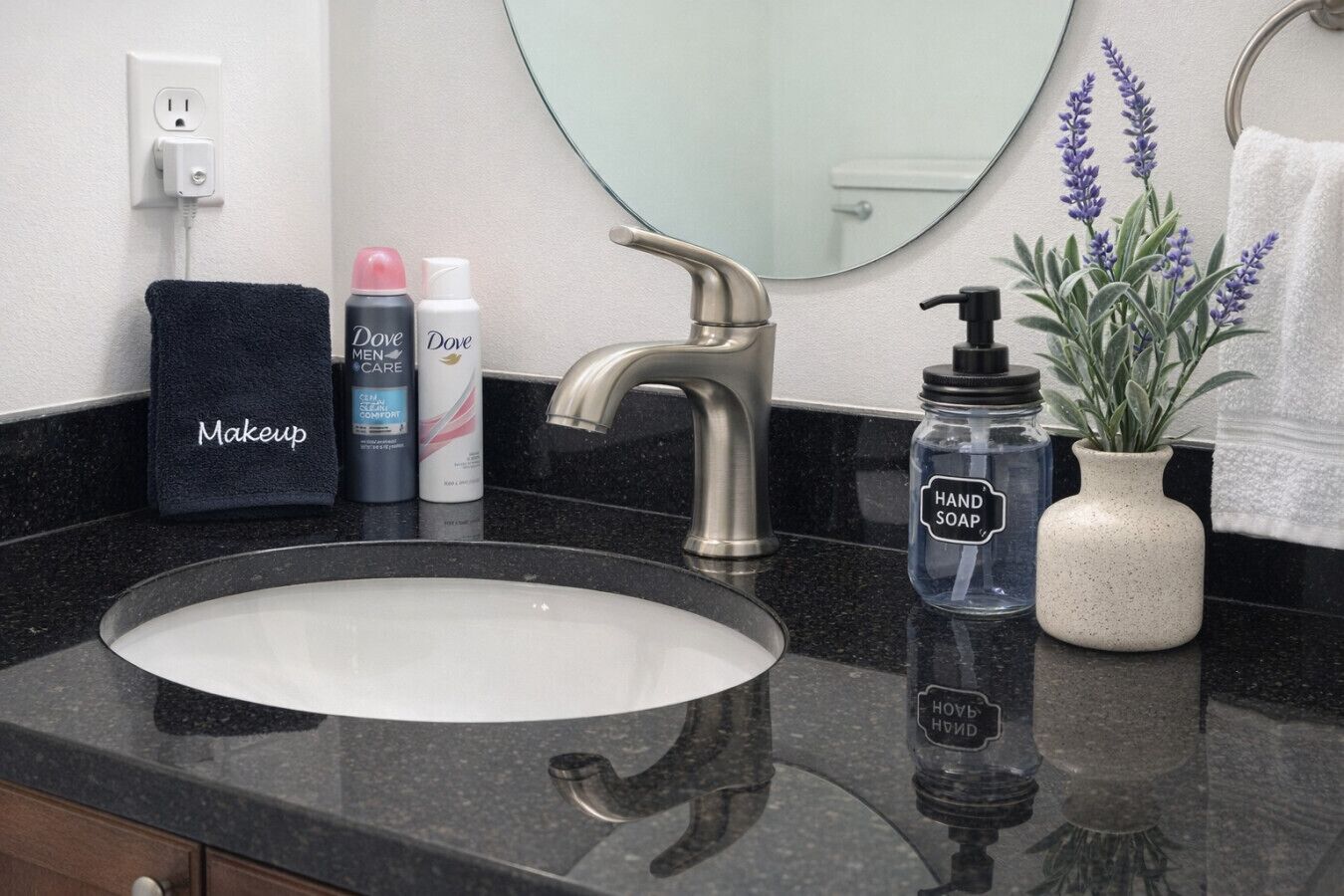 A bathroom with a sink, a mirror, a towel, Dove Men+Care products, a hand soap dispenser, and a potted plant.