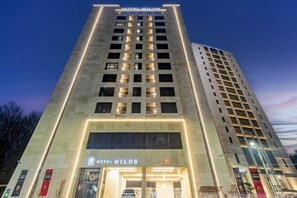 Un hôtel à plusieurs étages, doté d’une entrée imposante et d’une enseigne lumineuse.