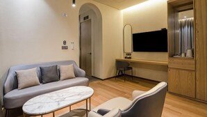 A modern hotel room with a sofa, a small table, a TV, a mirror, and a wooden cabinet. - Uiwang Milos Hotel (Uiwang-si)