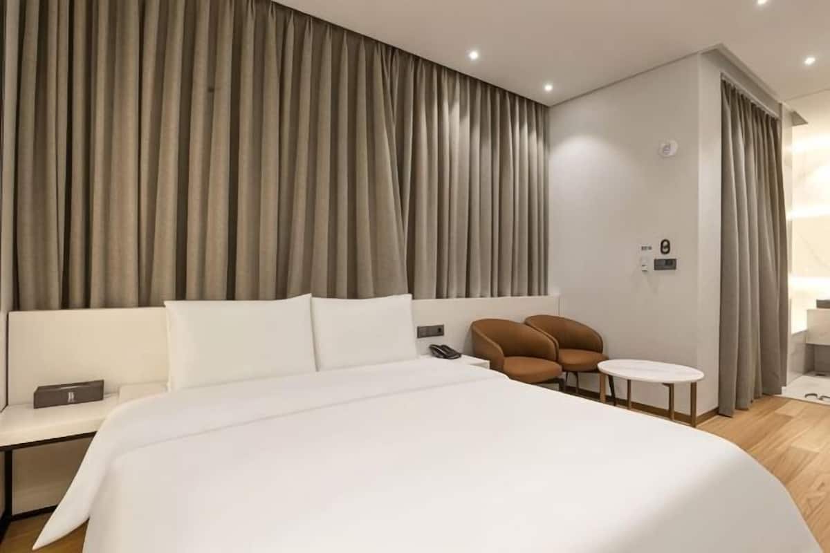 Een hotelkamer met een groot bed, een witte bank, een klein rond tafeltje en een bruine stoel.