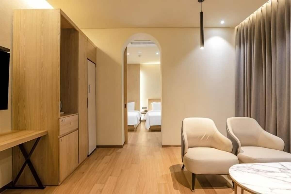 Een hotelkamer met een houten bureau, twee fauteuils, een tafeltje, een televisie en een bed op de achtergrond.