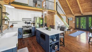 A spacious kitchen with wooden beams, a dining area, and a staircase leading to an upper level. - Arch Fun Cabin - Modern Cabin w/ Hot Tub, Games & Views (Stanton)