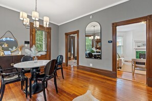 A dining area with a round table, black chairs, and a chandelier. There is a mirror on the wall and a wooden door leading to another room. - Second Street's Queen Ann (Lexington)