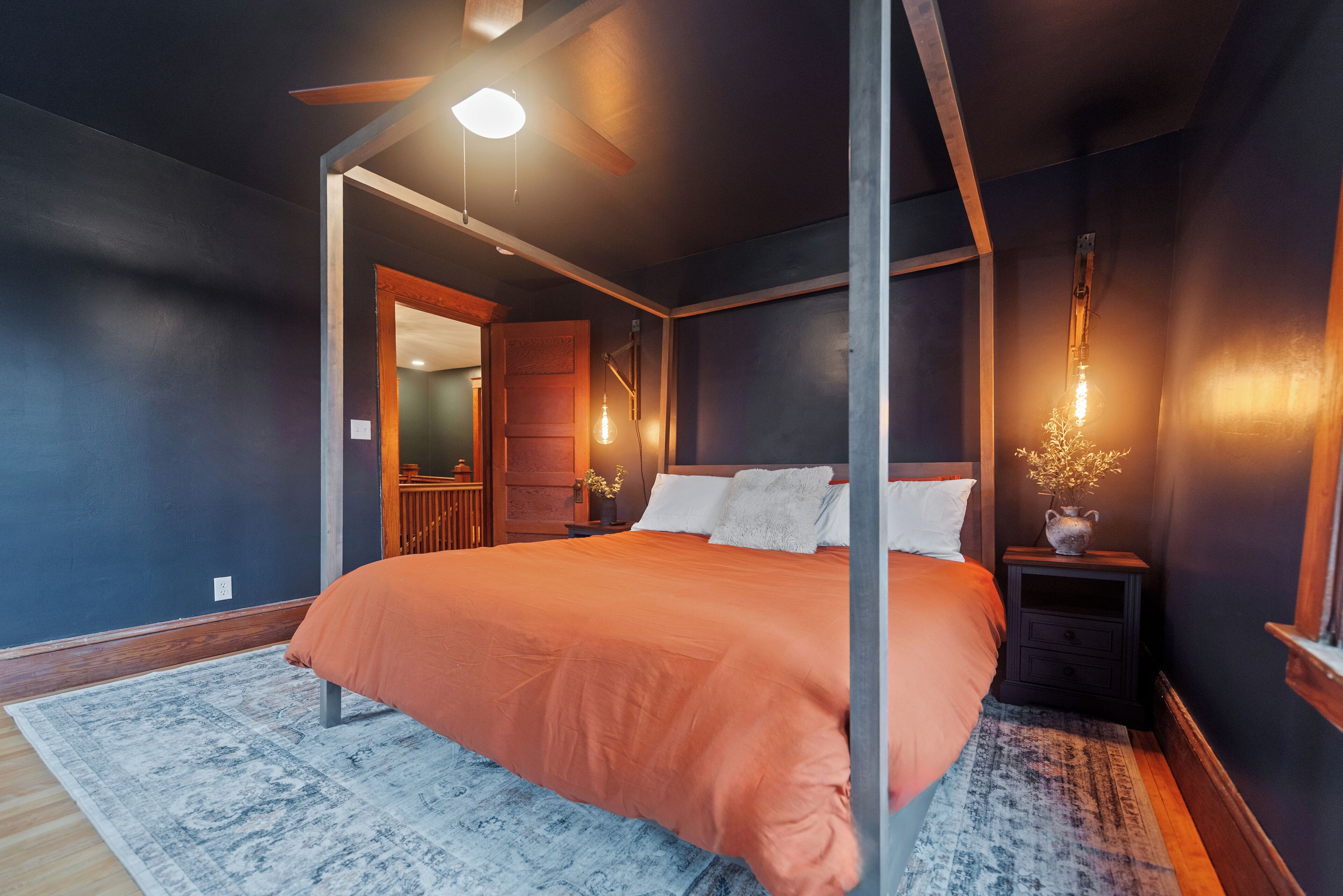 Quarto com cama, mesa de cabeceira, ventilador de teto e luz noturna.