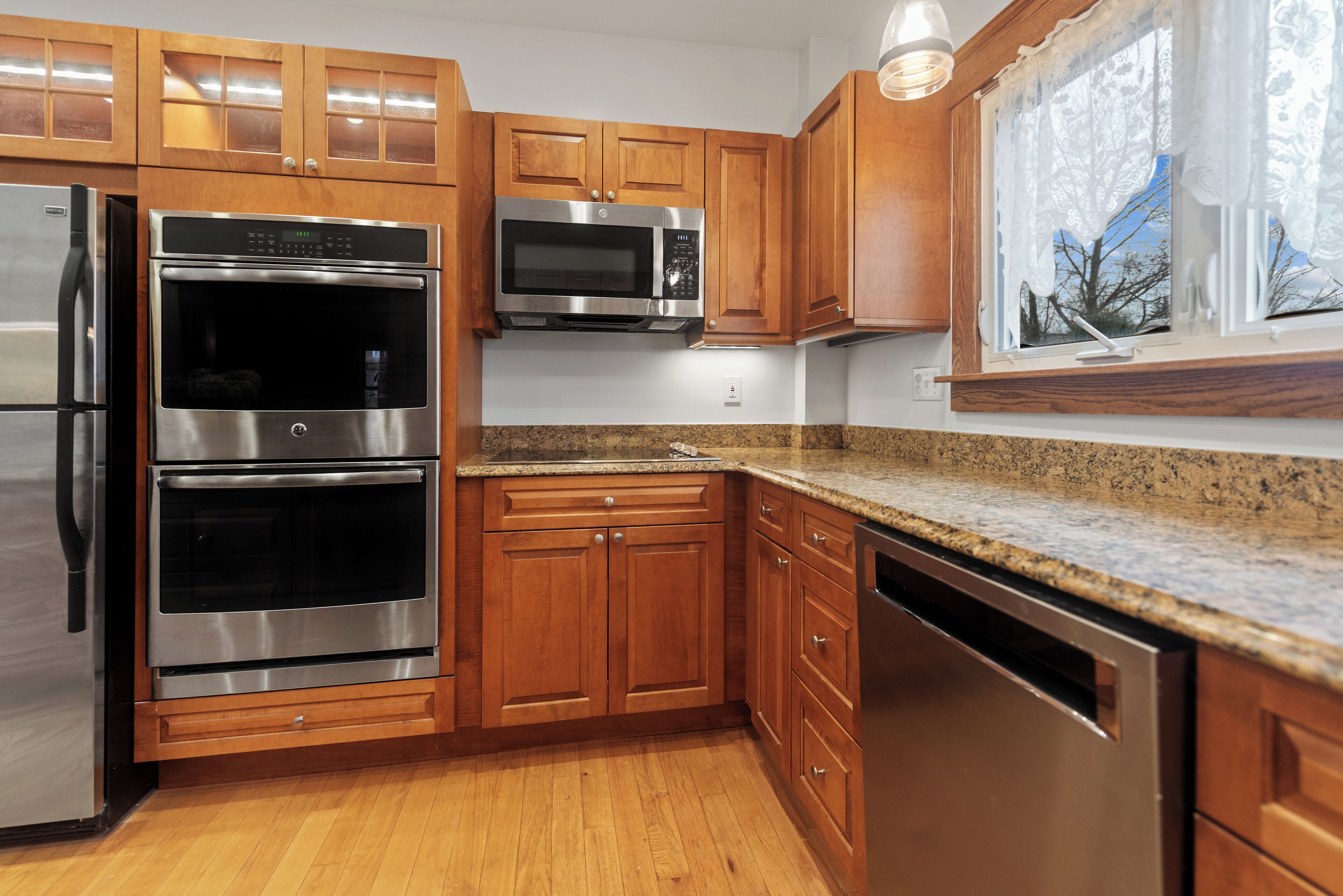 A kitchen with wooden cabinets, stainless steel appliances, granite countertops, and a window with a view.