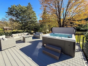 Un bain à remous sur une terrasse en bois, avec des meubles en osier et une vue sur les arbres.