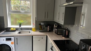 A modern kitchen with grey cabinets, a built-in dishwasher, a washing machine, a toaster, and a kettle.