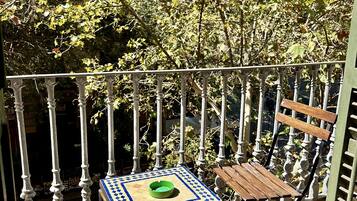 Un balcón con barandilla de metal, una mesa pequeña con un cuenco verde y un banco de madera.