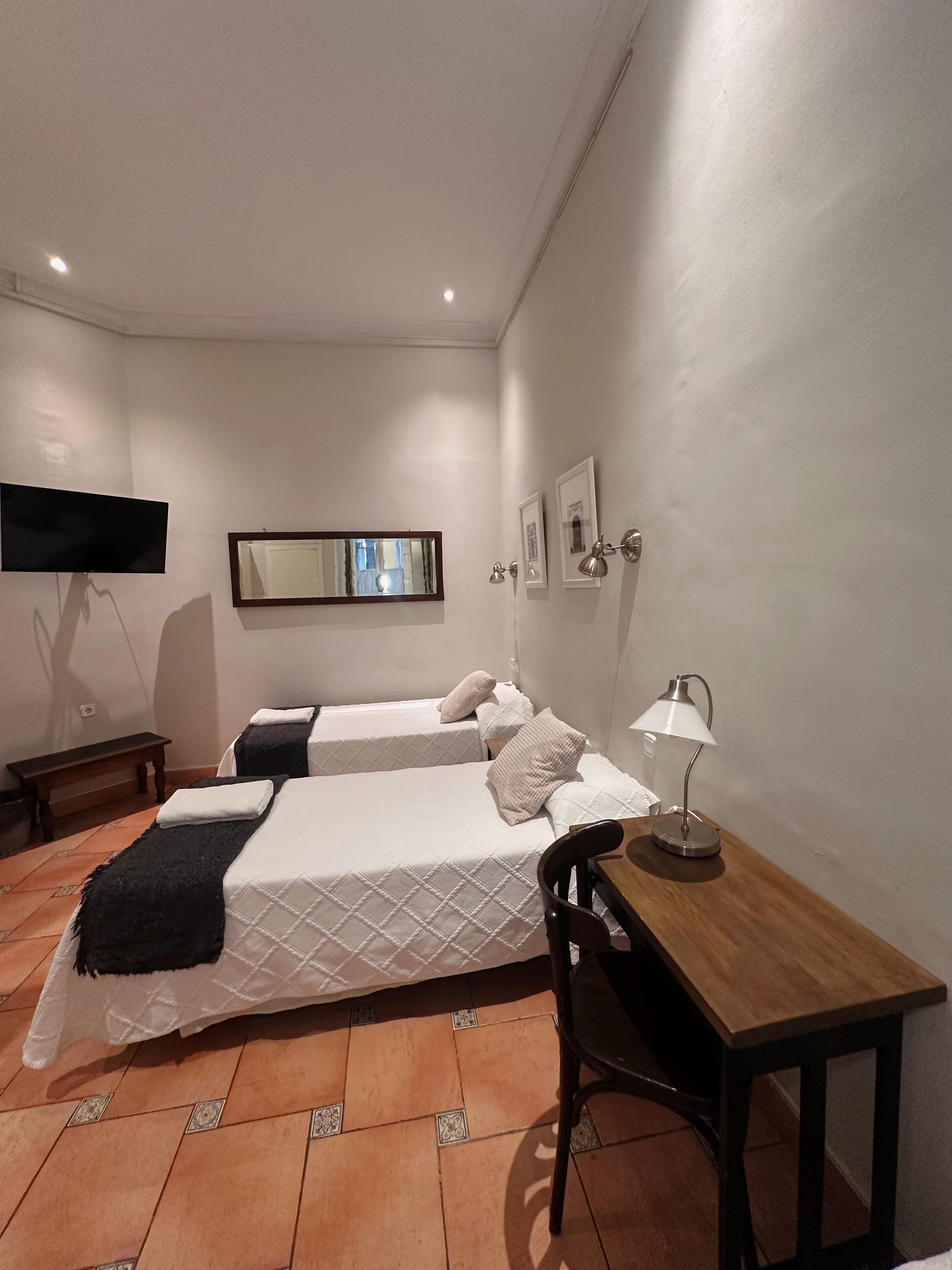 Habitación de hotel con dos camas, un escritorio, una silla, un televisor y un espejo.