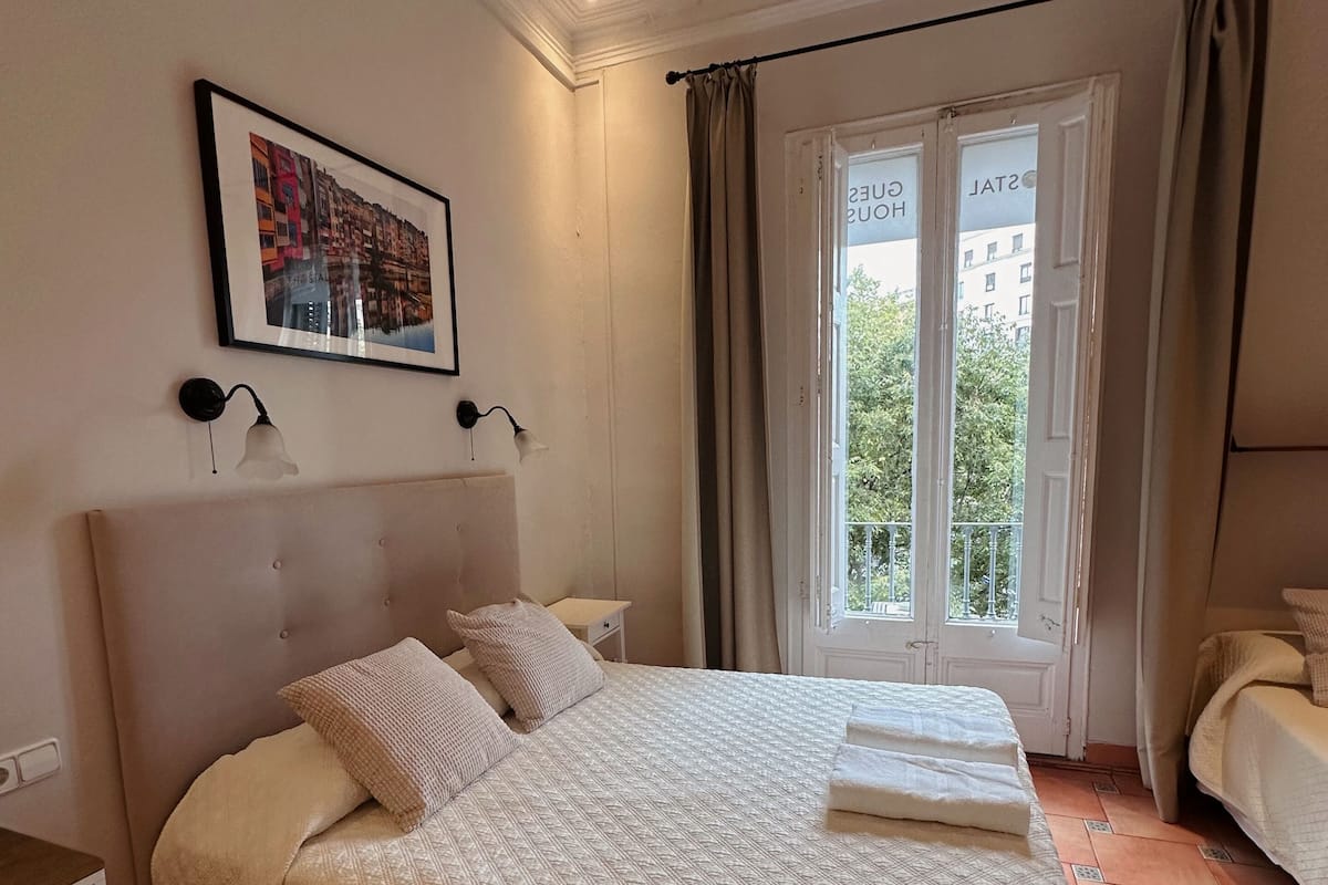 A hotel room with a large bed, a nightstand, a framed picture on the wall, and a window with curtains.