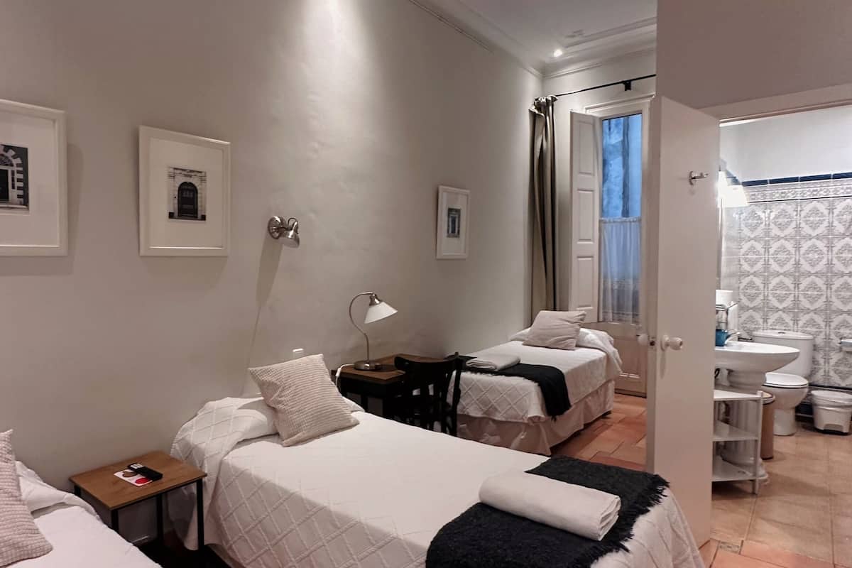 A hotel room with two beds, a nightstand, a desk, a chair, and a bathroom with a sink and toilet.