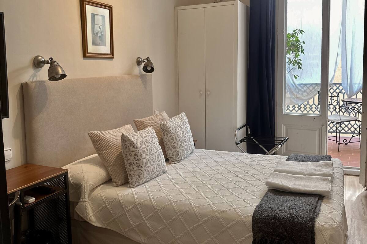 A bedroom with a large bed, a wardrobe, a desk, and a window with a view of the outside.