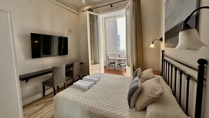 Une chambre d’hôtel comprenant un lit, un bureau, une chaise, une télévision et un balcon avec une table et des chaises.