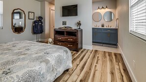 Ein Schlafzimmer mit Bett, Deckenventilator, Kommode, Schminktisch mit Spiegeln und Fernseher an der Wand.