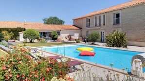 Ein Schwimmbad mit Liegestühlen, ein Gebäude mit Ziegeldach und ein gepflegter Garten.