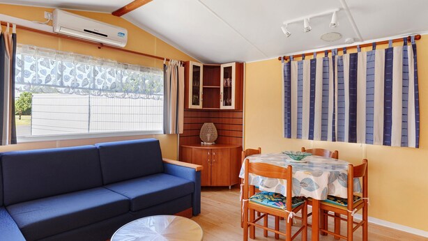 Ein Wohnzimmer mit einer Couch, einem Esstisch, Stühlen, einem Schrank und einer Klimaanlage.