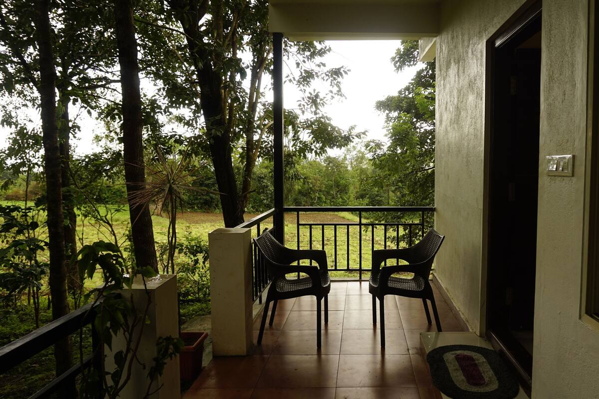 A balcony with two wicker chairs, a potted plant, and a view of a green landscape.