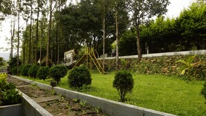 A playground with a slide and climbing structure surrounded by trees and a stone wall. - RAJ VILLAS (Chikkamagaluru)
