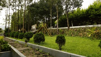 Un parque infantil con tobogán y estructura de escalada, rodeado de árboles y un muro de piedra.