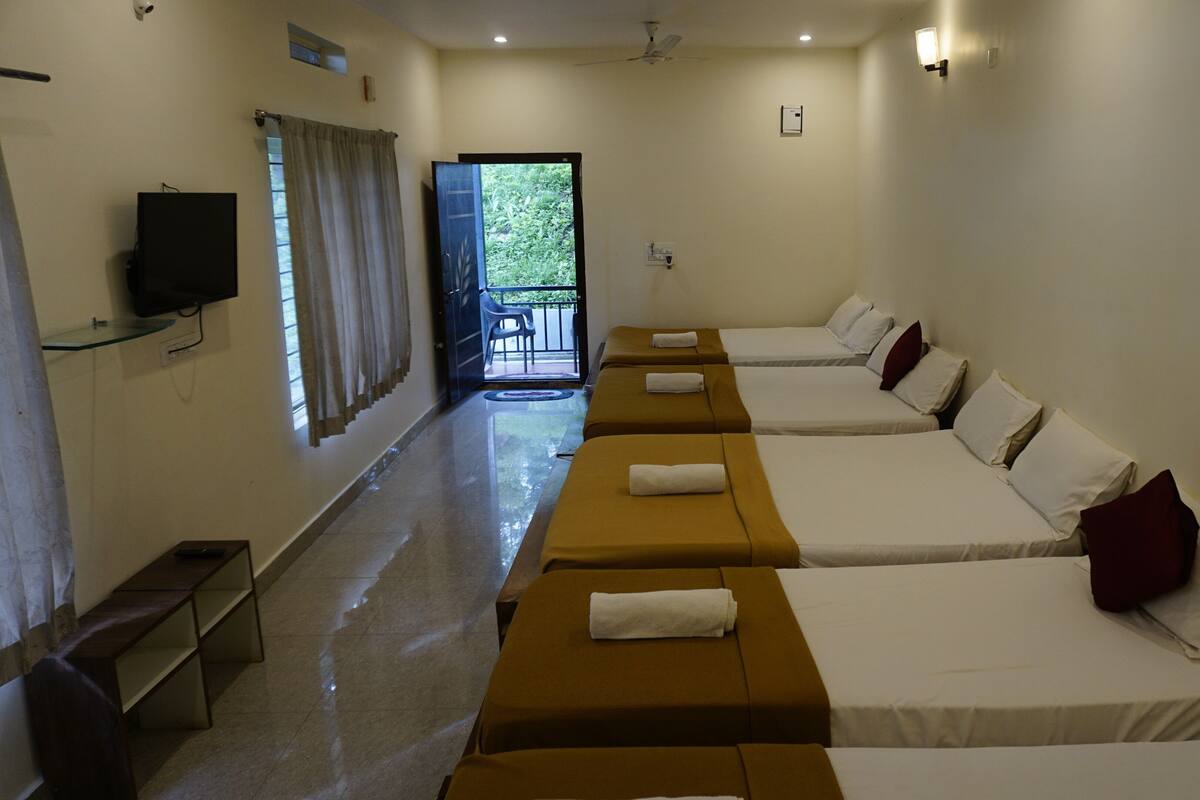 A hotel room with four single beds, a TV mounted on the wall, a balcony with a view, and a ceiling fan.