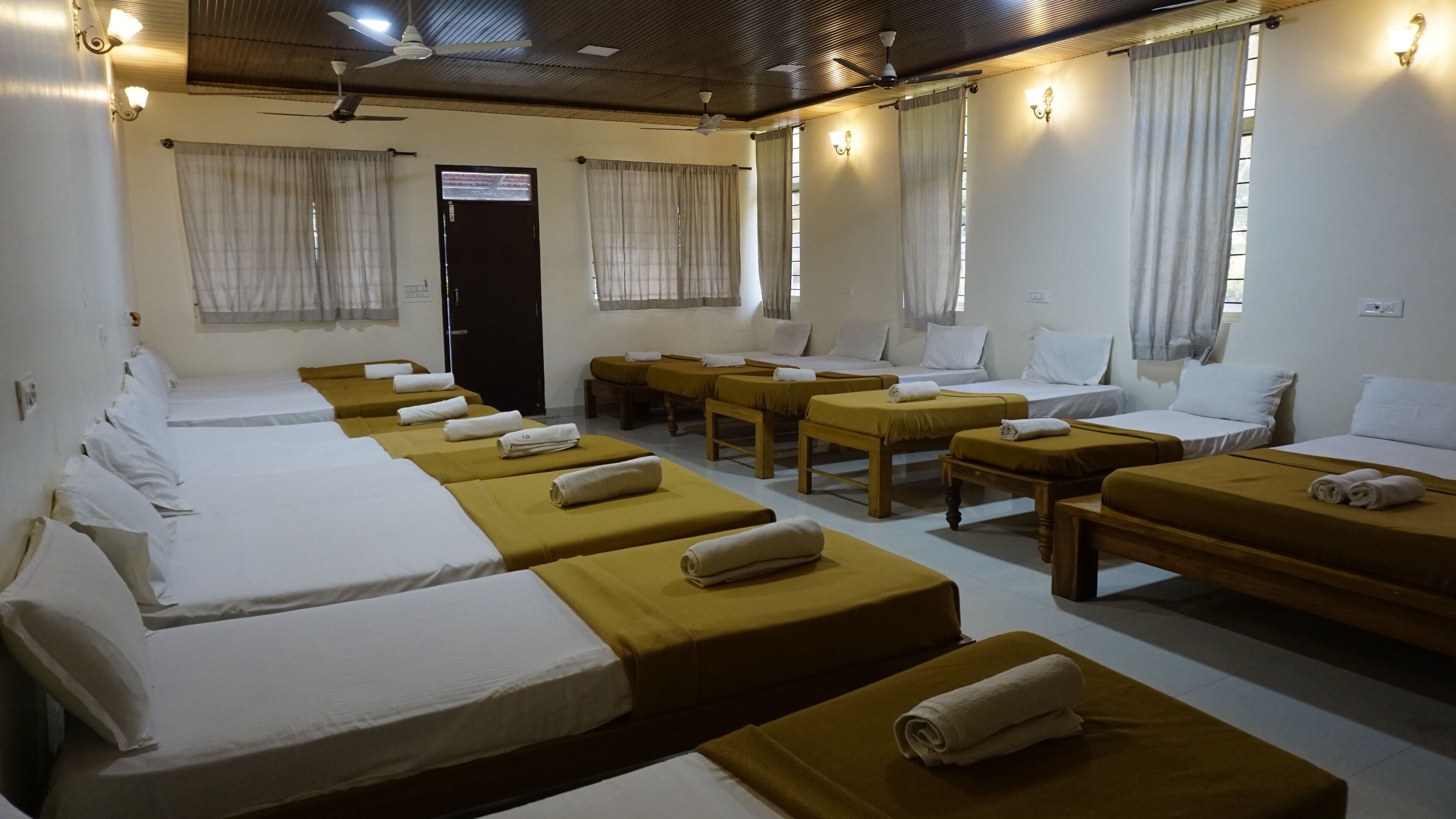 A hotel room with multiple beds, each with a rolled towel, and a small table in the center.