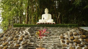 A large white statue of a seated figure on a stone platform surrounded by lush greenery. - RAJ VILLAS (Chikkamagaluru)