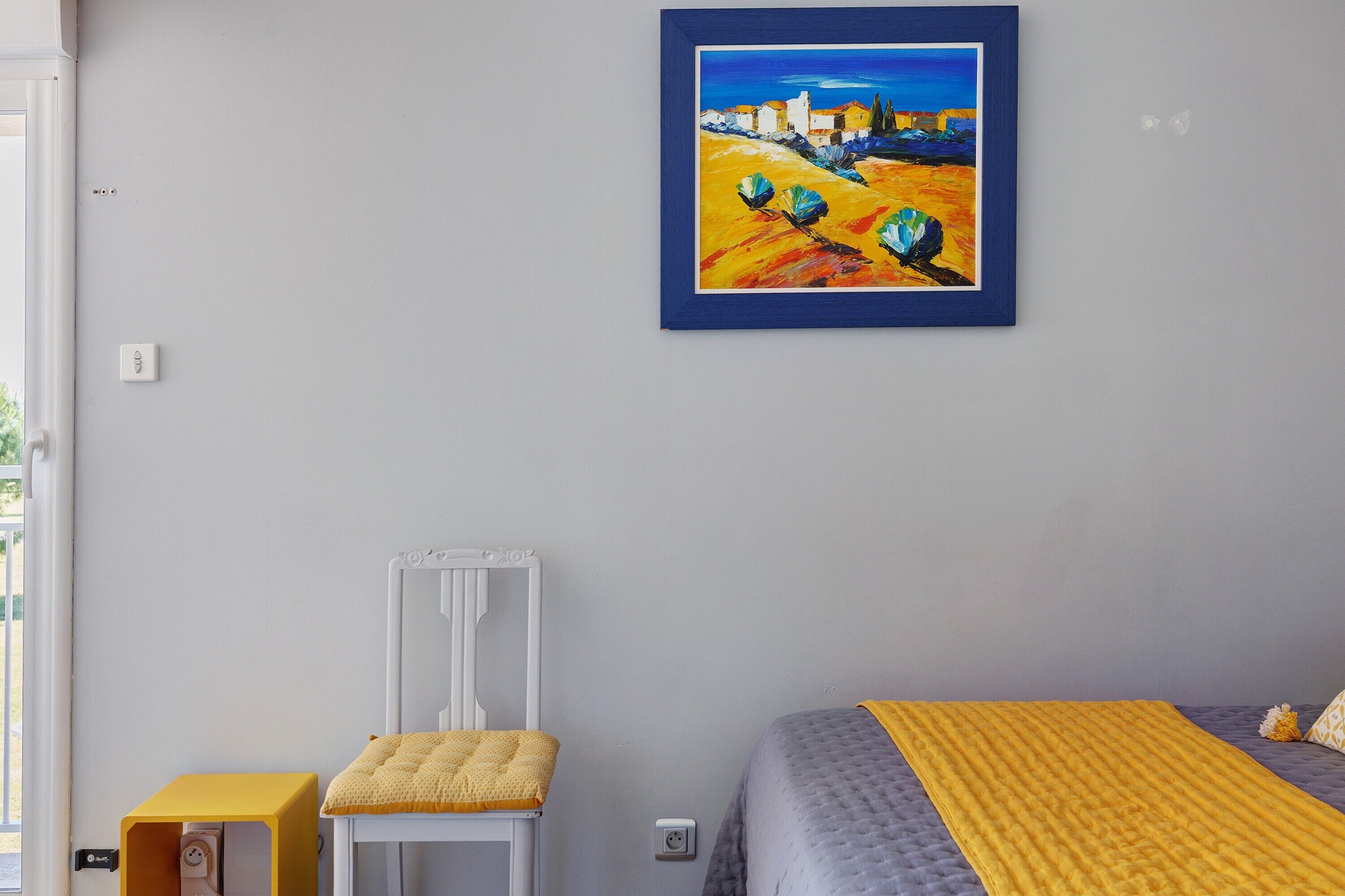 Un dormitorio con cama, una silla, una mesita y un cuadro en la pared.