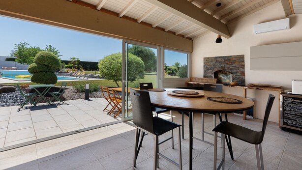 A modern kitchen with a large island, a dining area with chairs, and a view of a swimming pool. - Family Guest Room Near Futuroscope – Breakfast Included, Shared Pool (Neuville-de-Poitou)