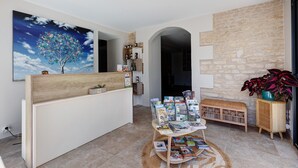 A reception area with a wooden desk, a wall-mounted painting of a tree, a stone wall, and a wicker bench. - Family Guest Room Near Futuroscope – Breakfast Included, Shared Pool (Neuville-de-Poitou)