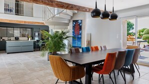 A spacious dining area with a modern table and chairs, a kitchen in the background, and a staircase leading to an upper level. - Family Guest Room Near Futuroscope – Breakfast Included, Shared Pool (Neuville-de-Poitou)