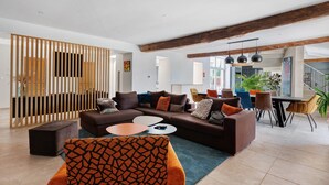 A modern living room with a sectional sofa, ottomans, a coffee table, and a dining area with chairs and a table. - Family Guest Room Near Futuroscope – Breakfast Included, Shared Pool (Neuville-de-Poitou)