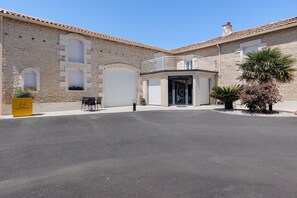 A stone building with a balcony, a garage door, and a palm tree. - Holiday Home La Gloriette (3 stars) in Neuville de Poitou with Pool (Neuville de Poitou)