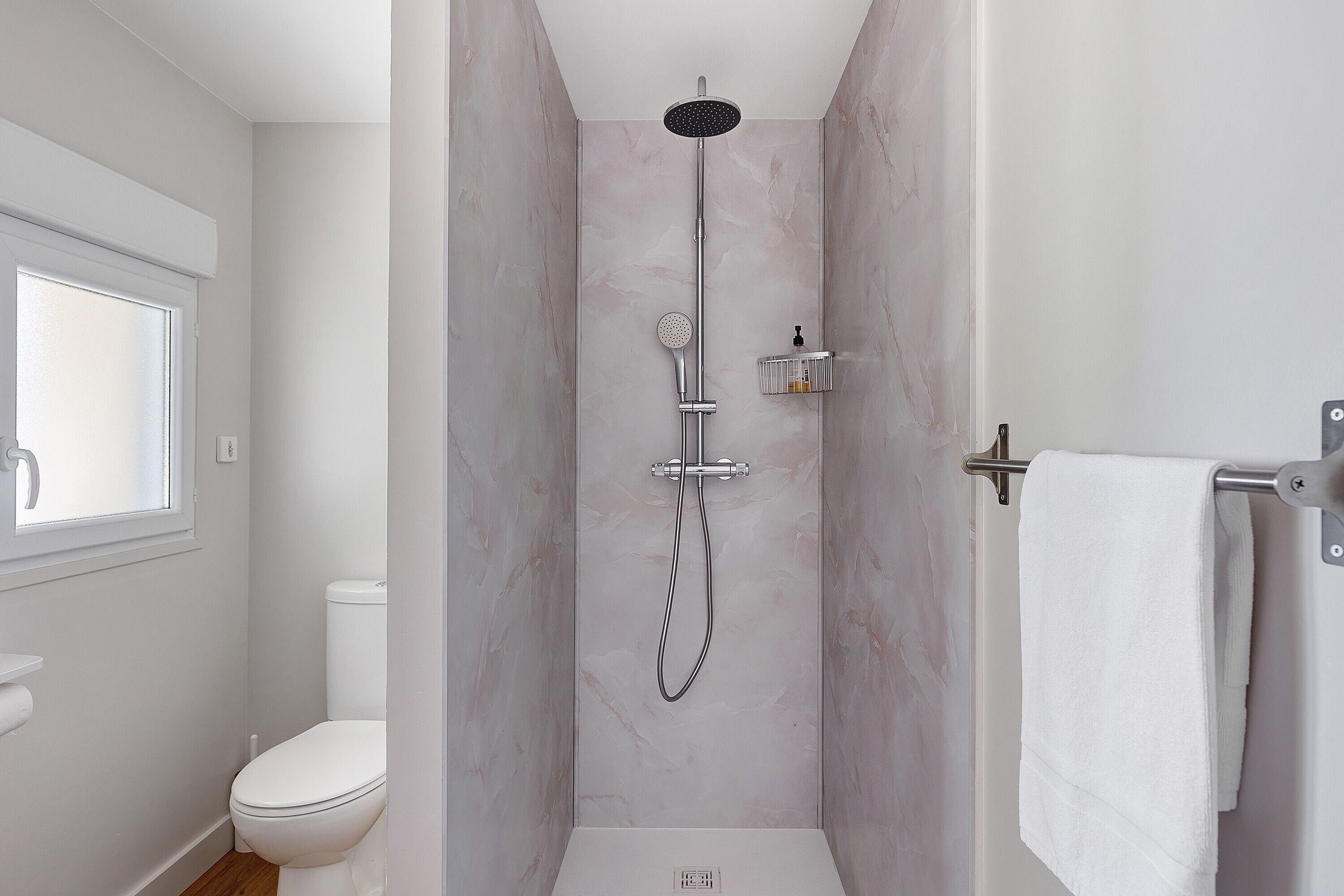 Een badkamer met een douche, toilet en een raam.