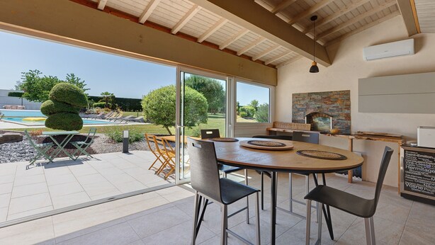Un comedor moderno con una mesa grande, sillas y vistas a una piscina y follaje.