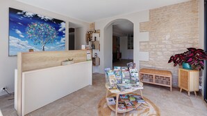 Un área de recepción con un escritorio de madera, un cuadro colgado en la pared que representa un árbol, una pared de piedra, un banco de mimbre y una mesa con revistas.