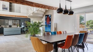 Una cocina moderna con una isla grande, un comedor con sillas coloridas y una escalera que sube a un nivel superior.