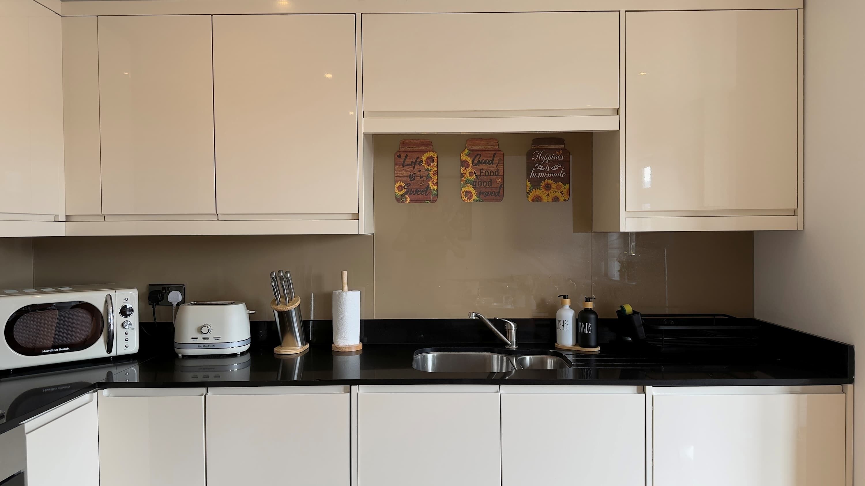 A modern kitchen with white cabinets, a black countertop, a microwave, a toaster, and a sink.
