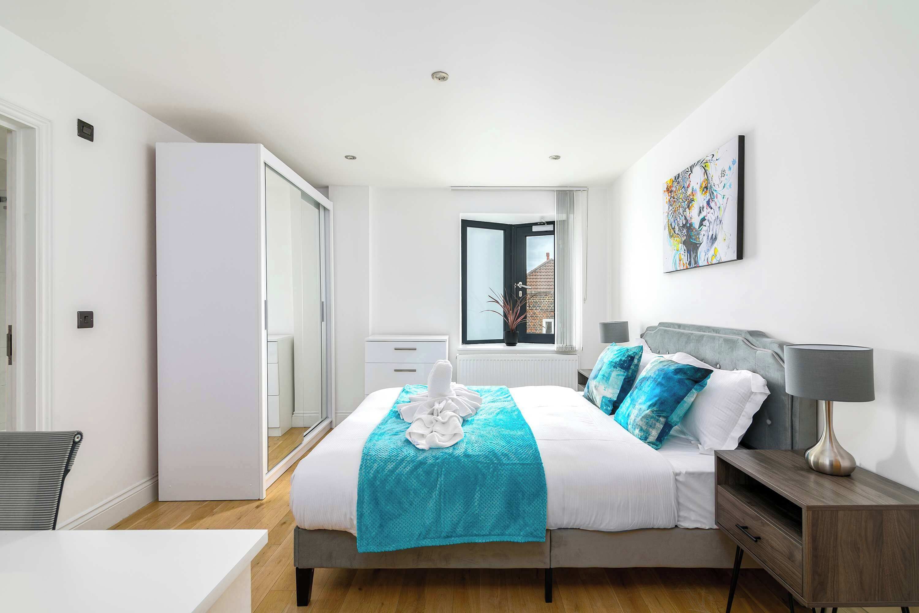 A modern bedroom with a bed, bedside table, lamp, and a window with a view of a building.