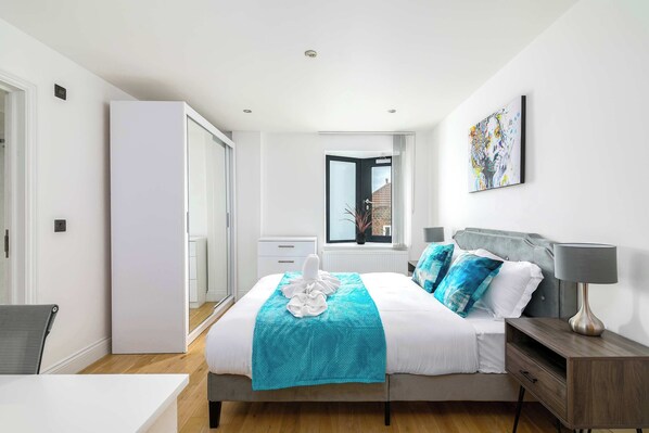 A modern bedroom with a bed, bedside table, lamp, and a window with a view of a building.