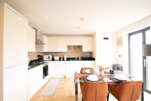 A modern kitchen with white cabinets, a dining table with orange chairs, and a large window providing natural light.