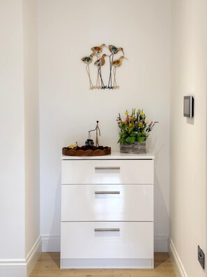 Ein weißes Schränkchen mit Schubladen, ein an der Wand befestigter Lichtschalter und ein dekoratives Wandbild.