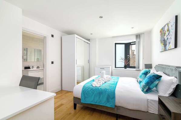 Une chambre à coucher moderne avec un lit, un bureau, une chaise, une fenêtre et un tableau accroché au mur.